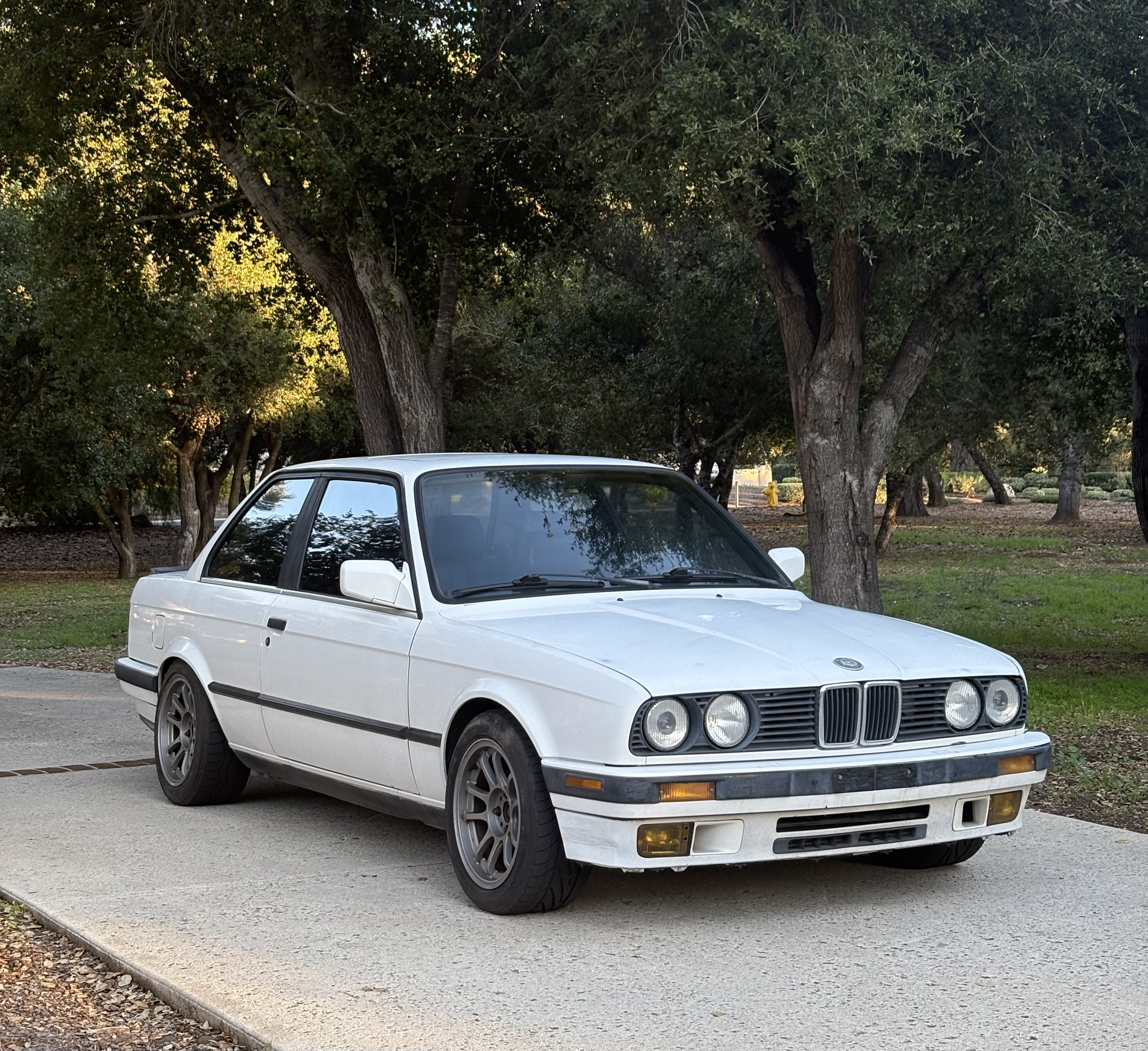 White BMW E30 in a driveway.